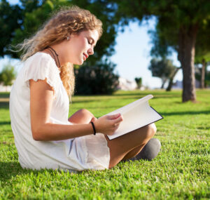 young woman reading a book at park on sunny day